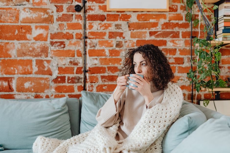 Woman wrapped in a blanket with a warm drink, relaxing at home