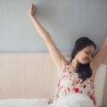 Woman waking up gently and stretching in bed feeling refreshed in the morning
