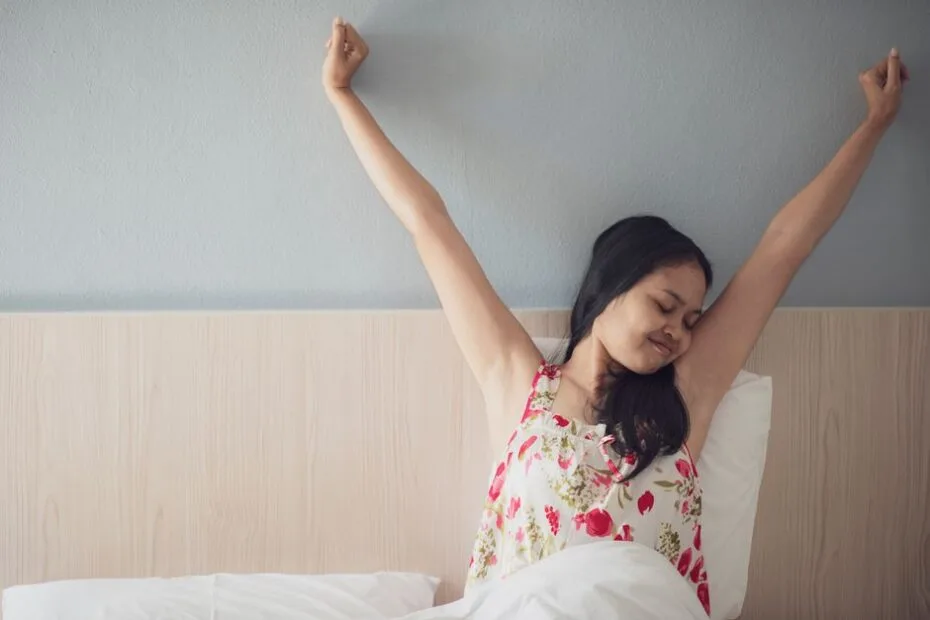 Woman waking up gently and stretching in bed feeling refreshed in the morning