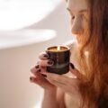 Woman relaxing while holding and smelling a lit scented candle