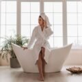 Woman relaxing in a plush white cozy robe in a calm, spa-like bathroom