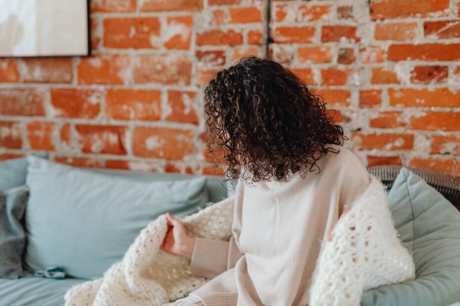 Woman wrapped in a cozy blanket on the couch, staying warm at home