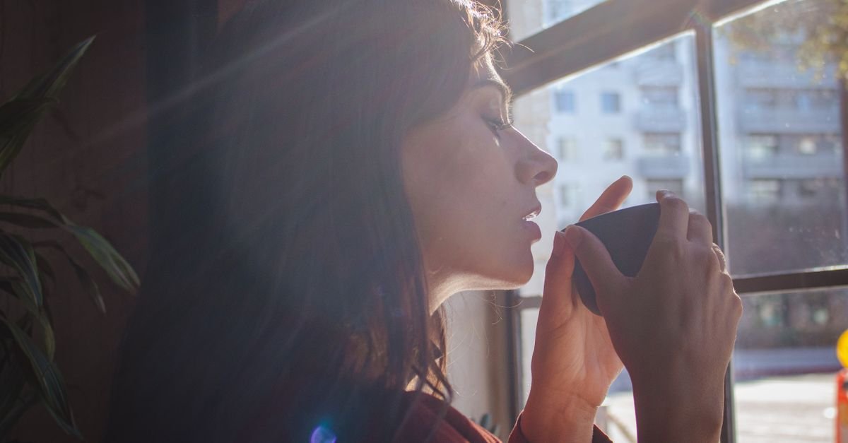 A woman drinking coffee by a sunlit window