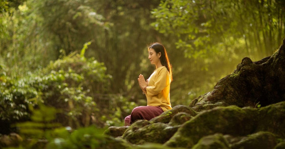 Woman meditating outdoors surrounded by green nature