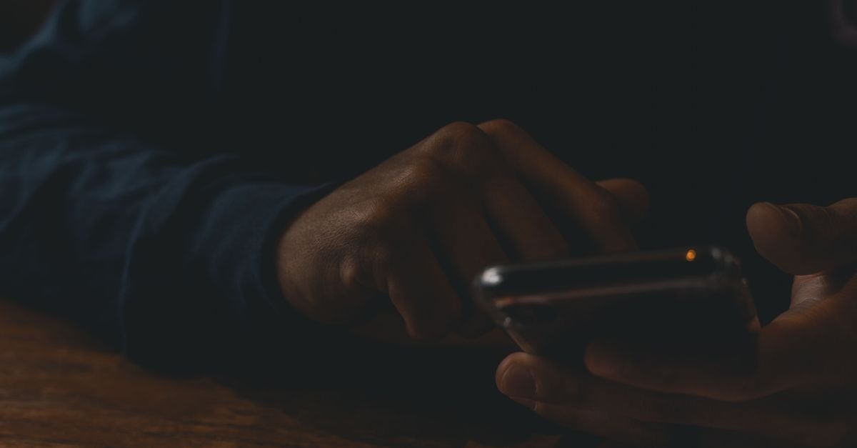 Hands scrolling a glowing phone in a dark room