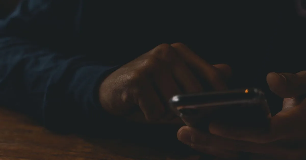 Hands scrolling a glowing phone in a dark room