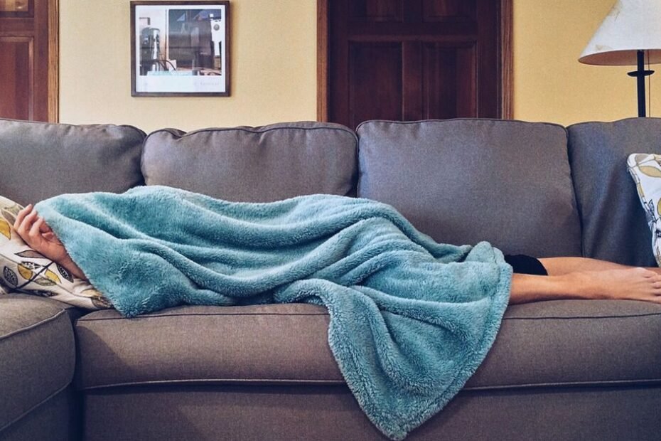 A woman napping under a blue blanket on a couch