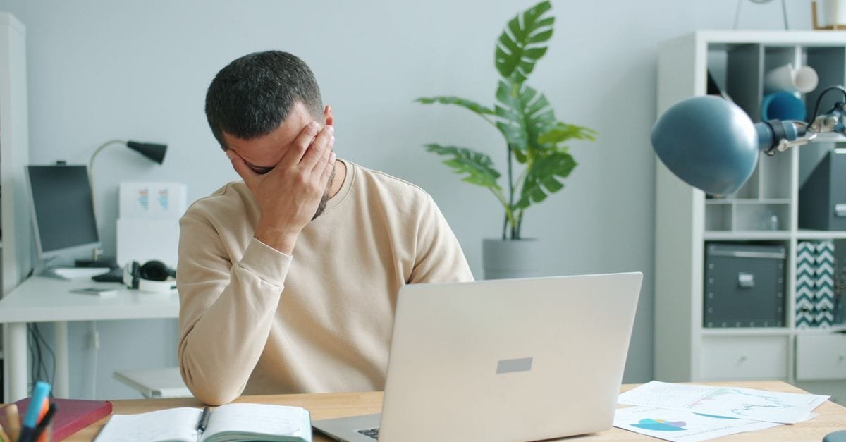 A man at a laptop holding his head in his hand