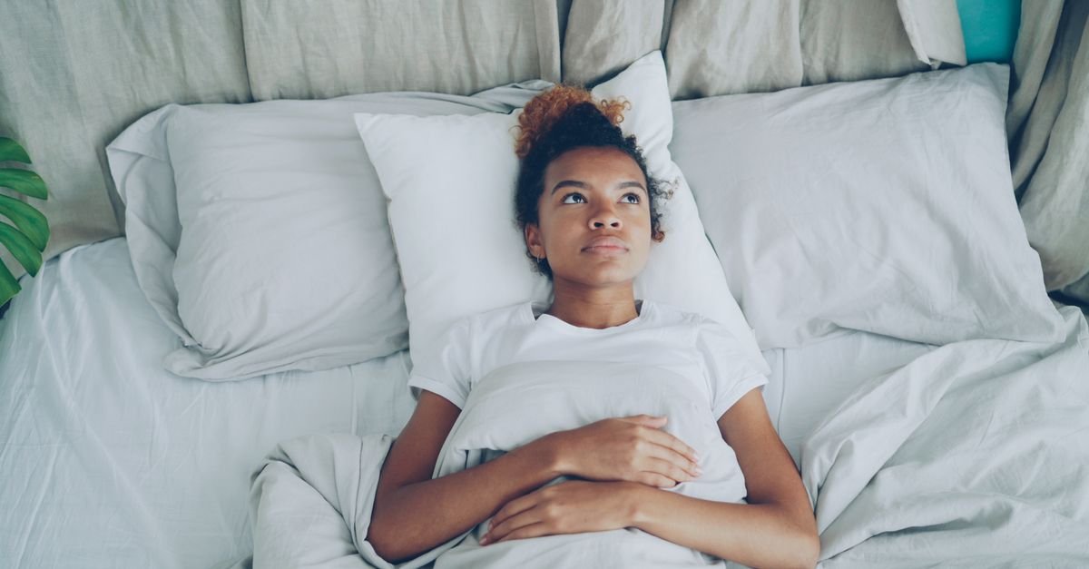 A woman lying awake in bed with a hand on her chest