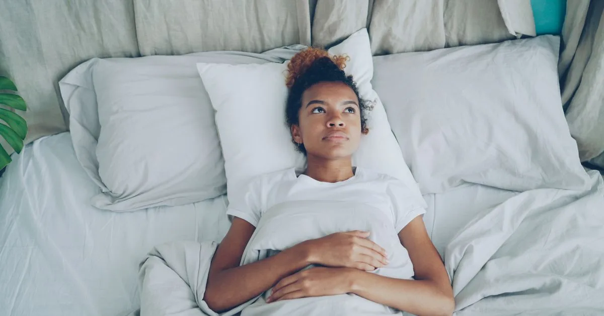 A woman lying awake in bed with a hand on her chest
