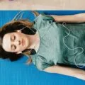 A woman lying on a yoga mat with headphones doing a guided meditation