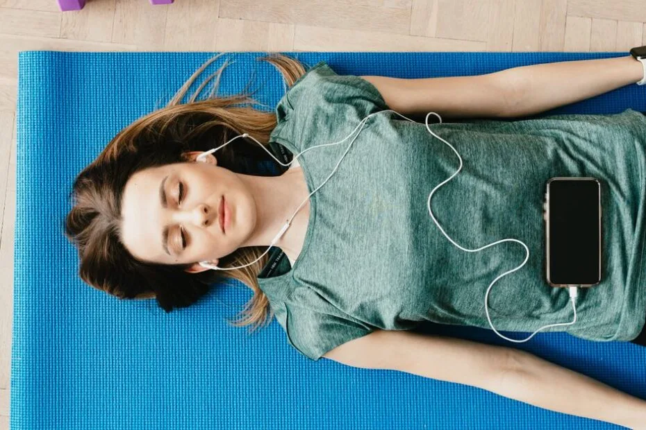 A woman lying on a yoga mat with headphones doing a guided meditation