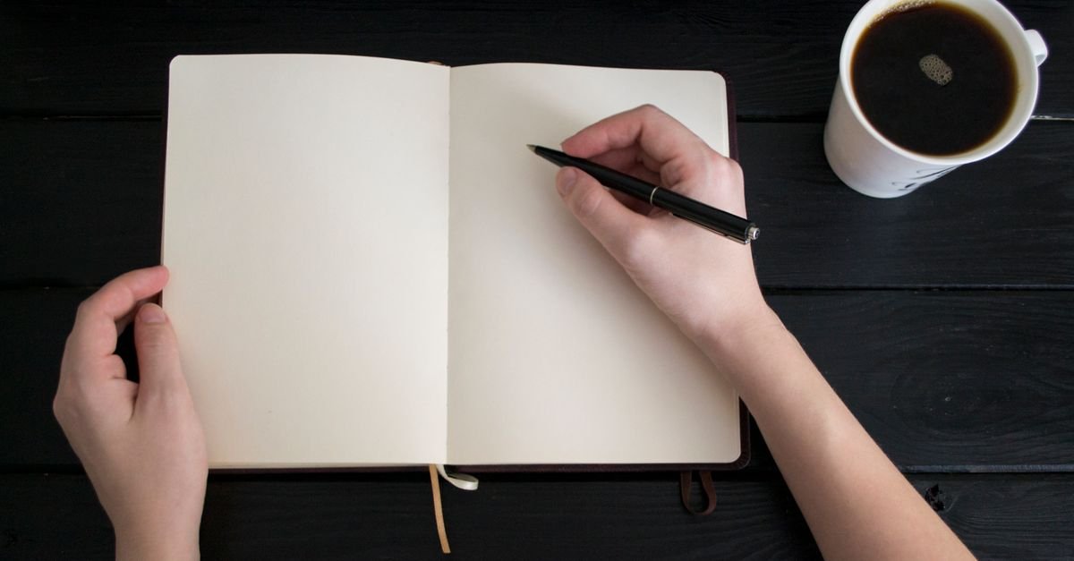 Hands writing in a journal beside a cup of coffee