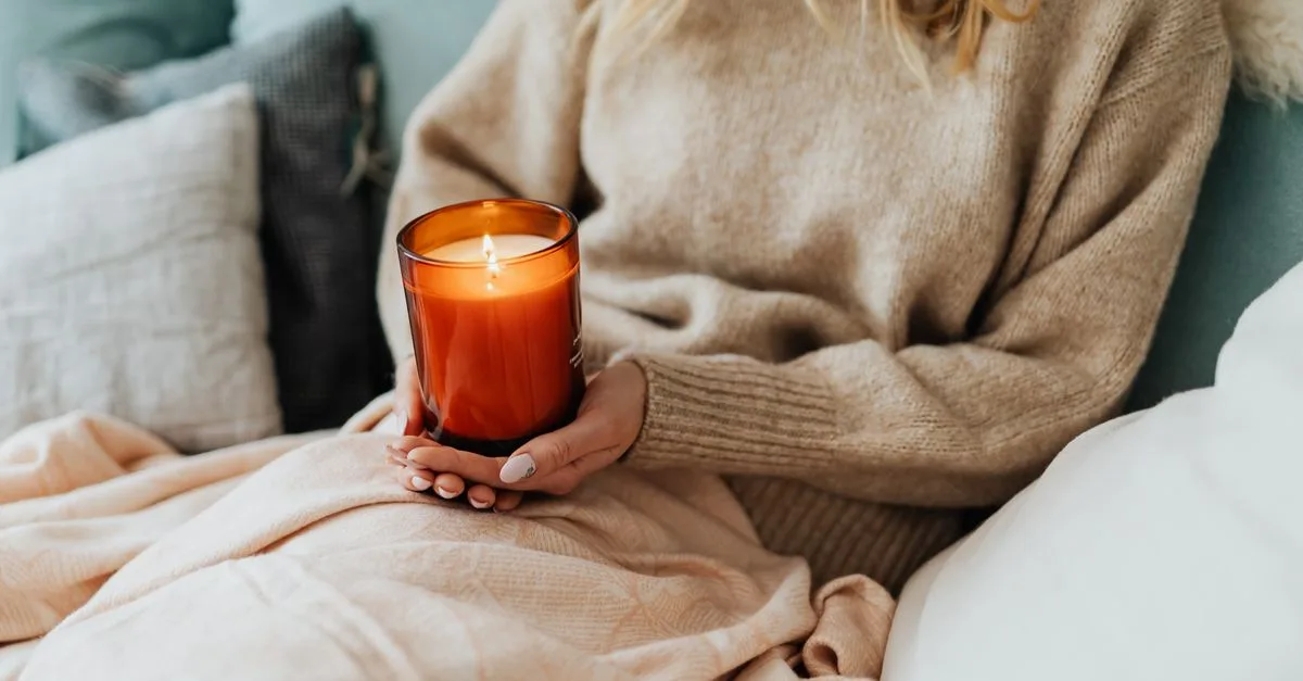 A person in a cozy sweater holding a lit candle