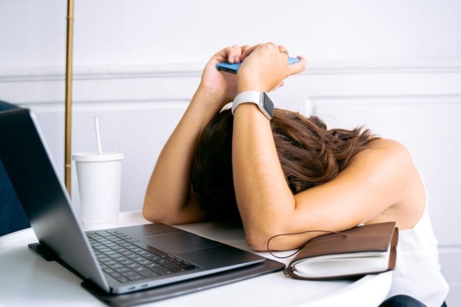 A woman resting her head on her desk beside a laptop, overwhelmed