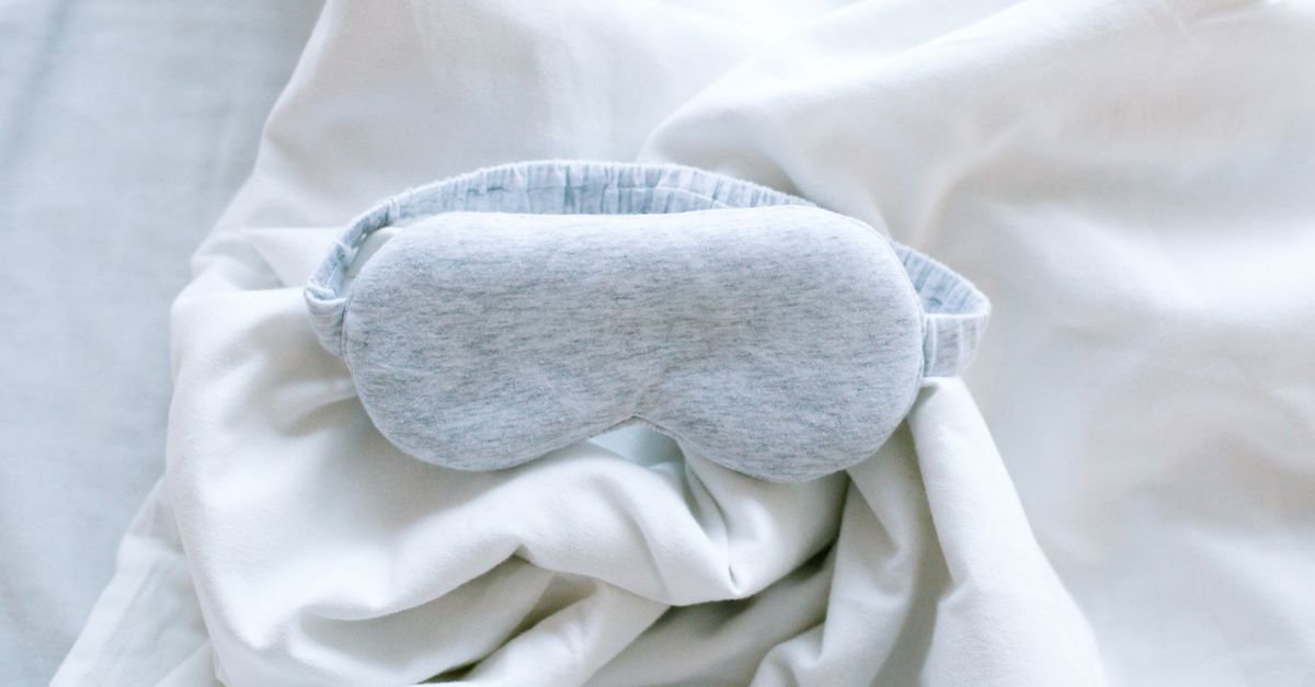A grey sleep mask lying on white bedding