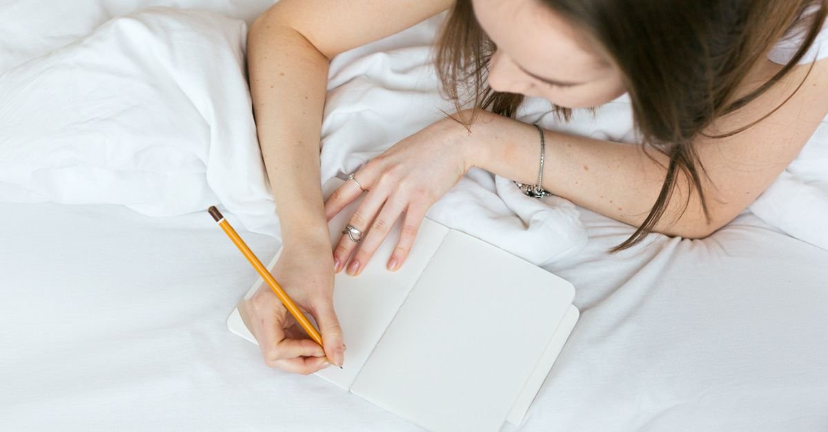 Woman writing in a journal while relaxing in bed