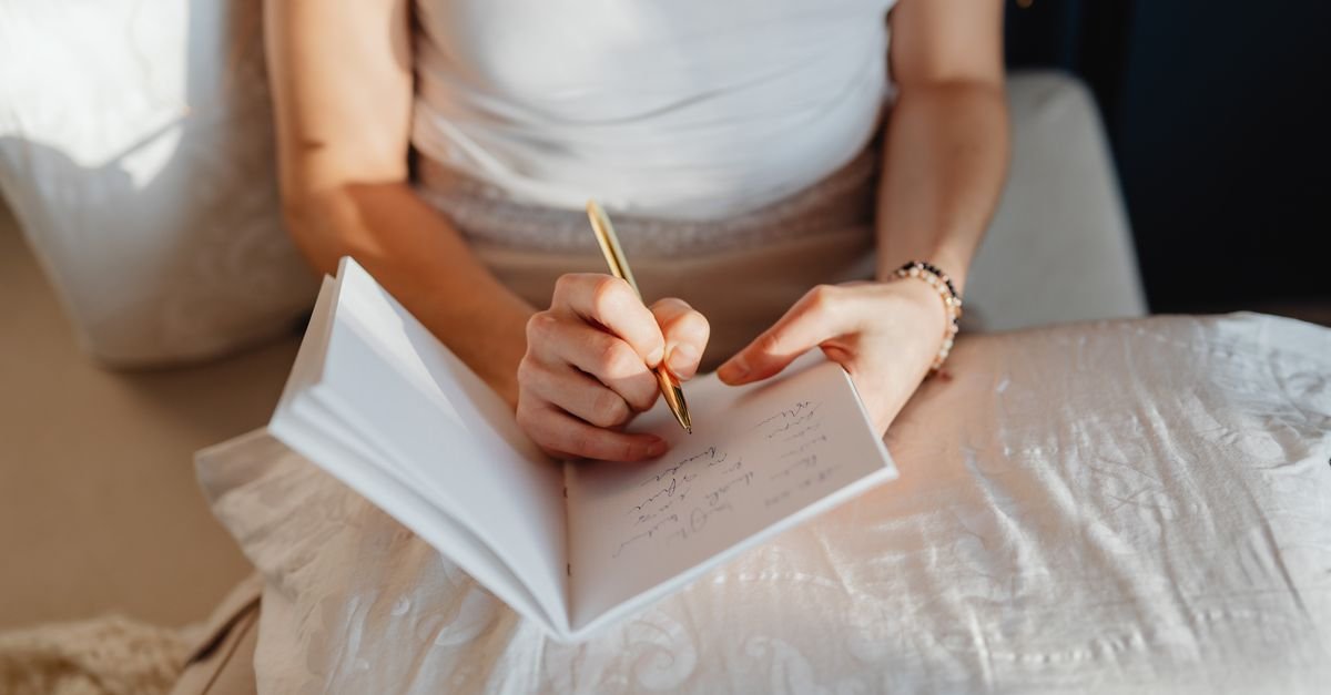 A woman writing in a journal on white bedding