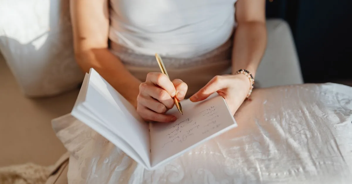A woman writing in a journal on white bedding
