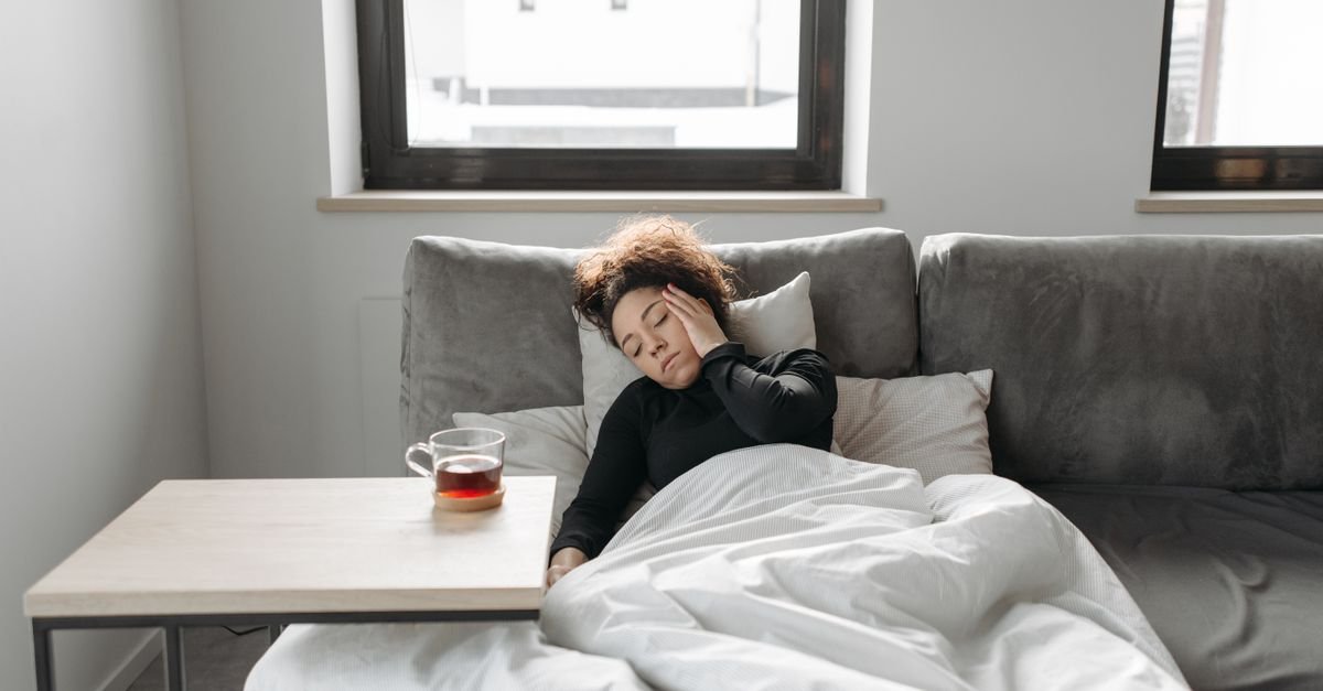 A woman resting under a duvet on a sofa in daylight