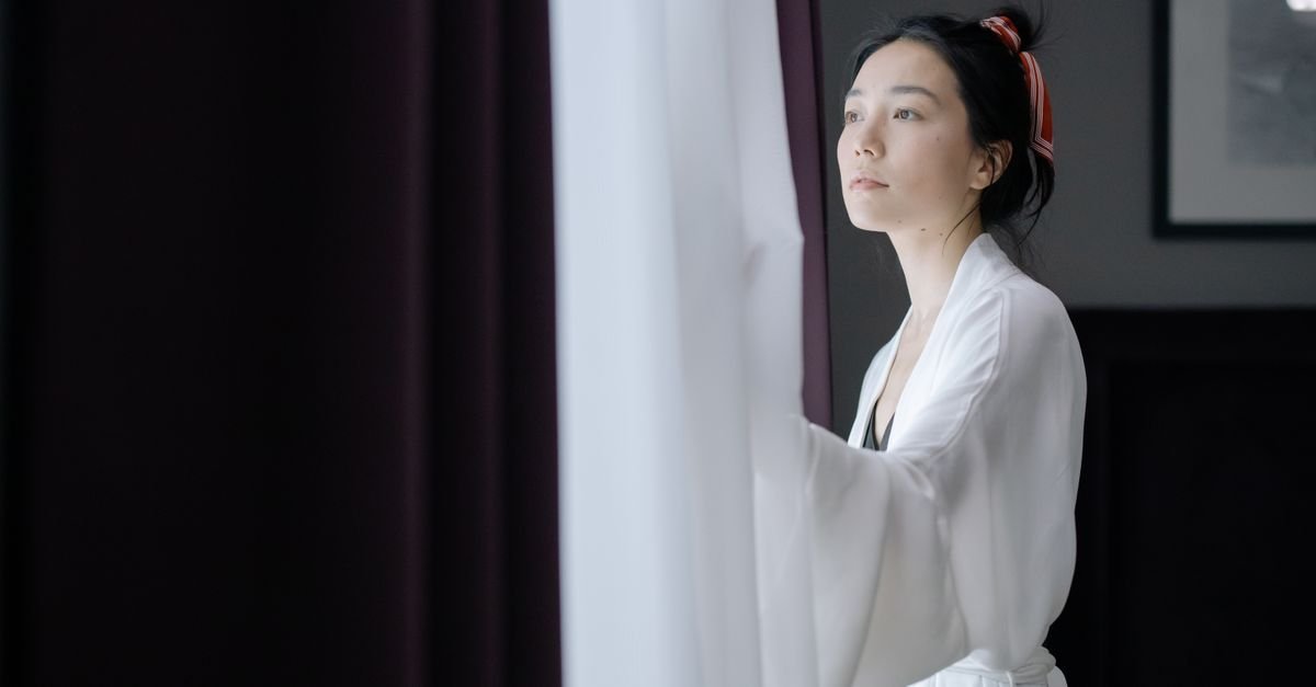 A woman opening the curtain at a bright window