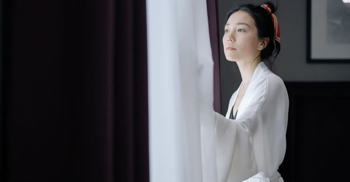 A woman opening the curtain at a bright window