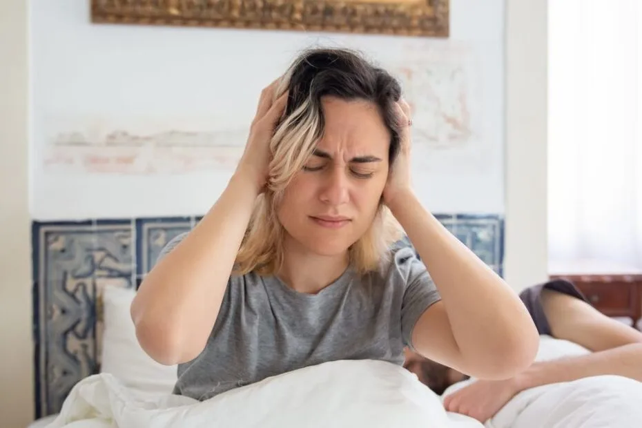 A woman sitting up in bed holding her head after waking