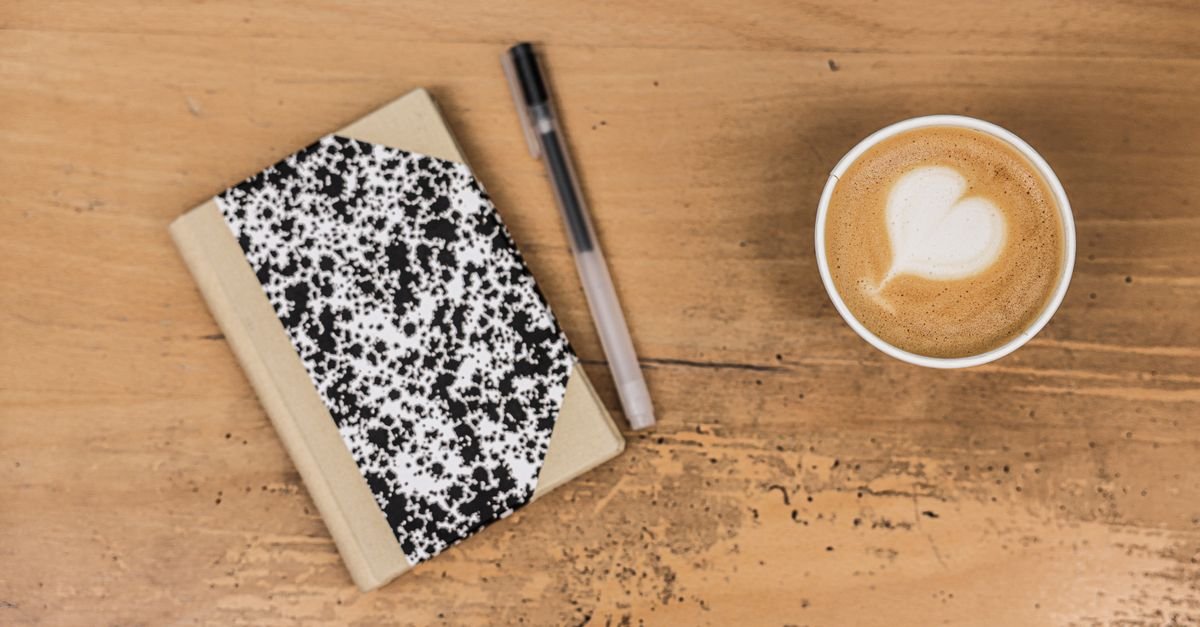 A journal and pen beside a cup of coffee on a wooden desk