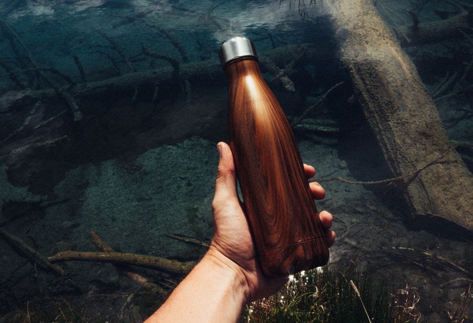 A wood-grain insulated water bottle held outdoors by water
