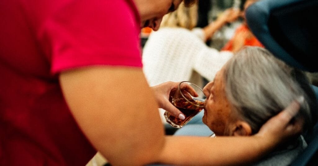A caregiver helping an older woman with tea